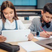 two kids using tablet and laptop to do homework